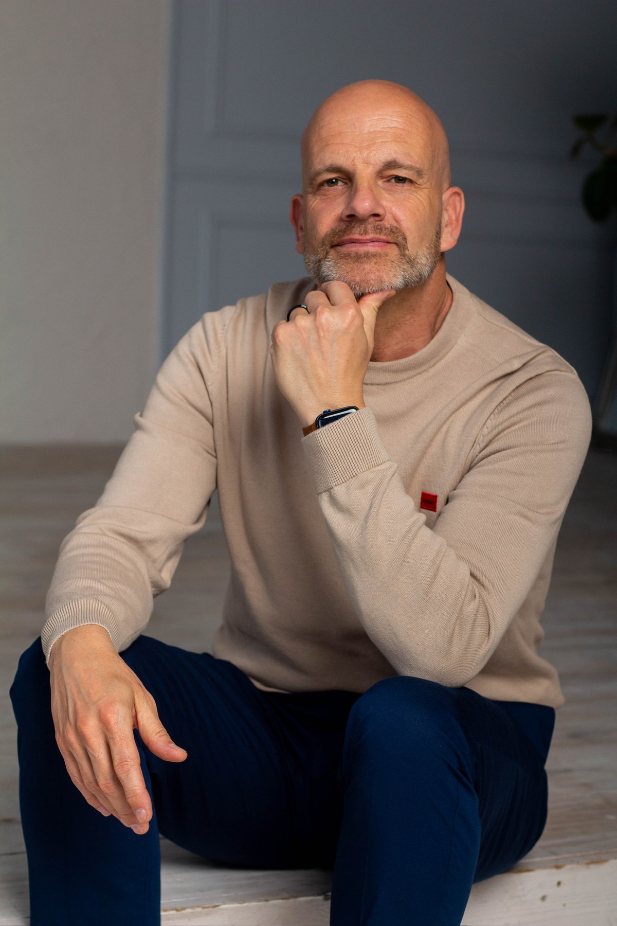 Thorsten Enderlin sitzt entspannt am Boden, die Hand am Kinn, und blickt in die Kamera